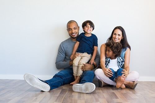 A smiling family of four sits together on the floor.